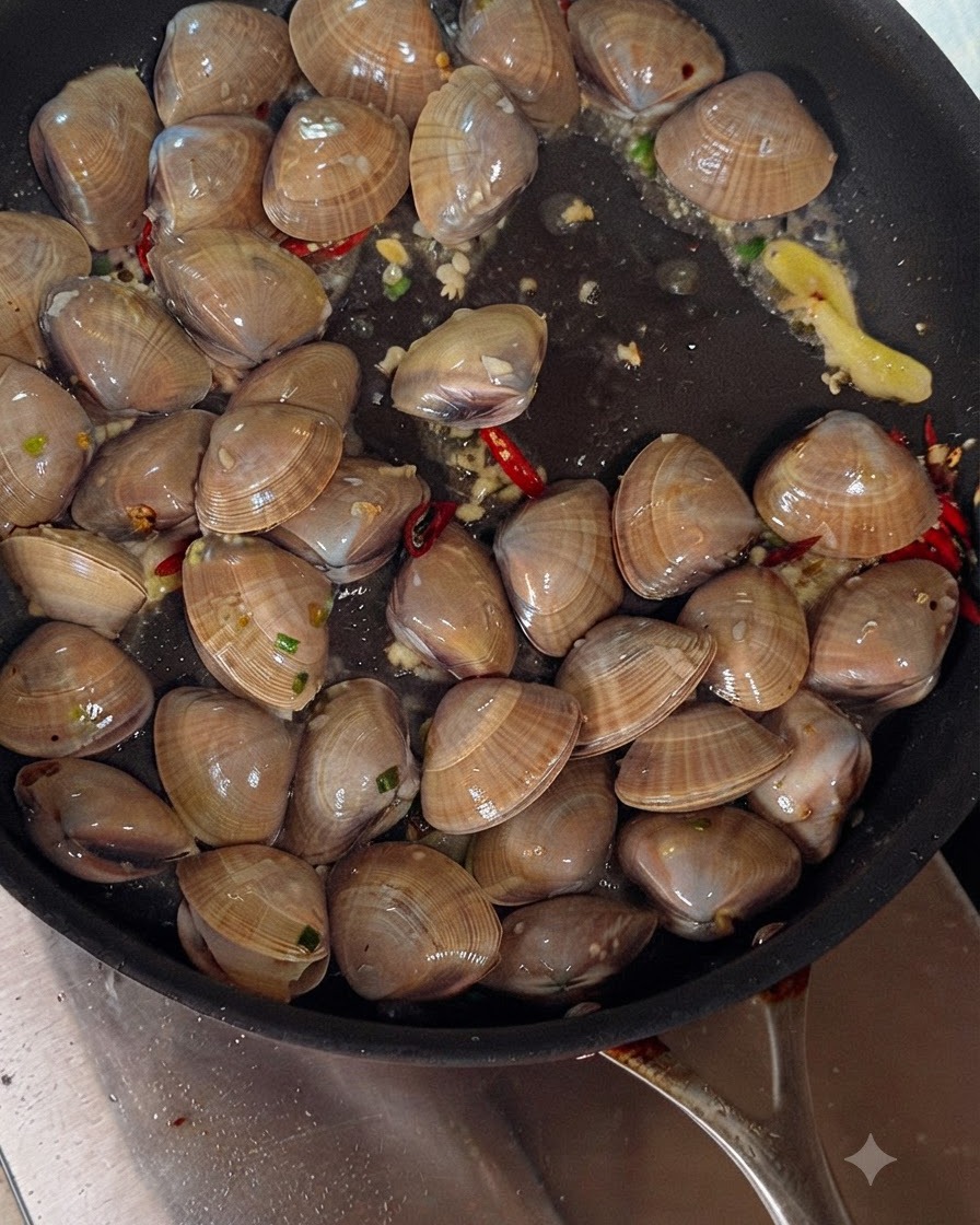 Vin blanc versé dune bouteille dans une poêle grésillante remplie de palourdes, dail et de piments.