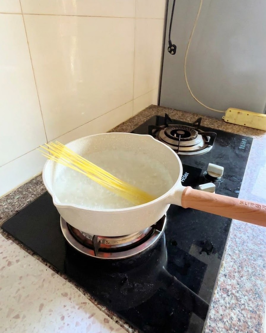 Nouilles de spaghetti sèches placées en diagonale dans une casserole deau bouillante sur une cuisinière.
