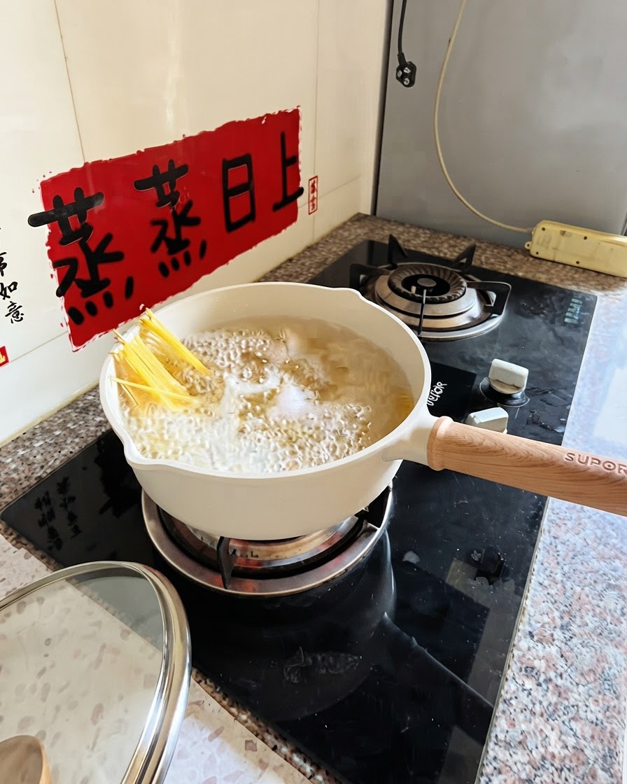 Spaghetti bouillant dans une casserole blanche avec des pinces submergeant partiellement les nouilles.
