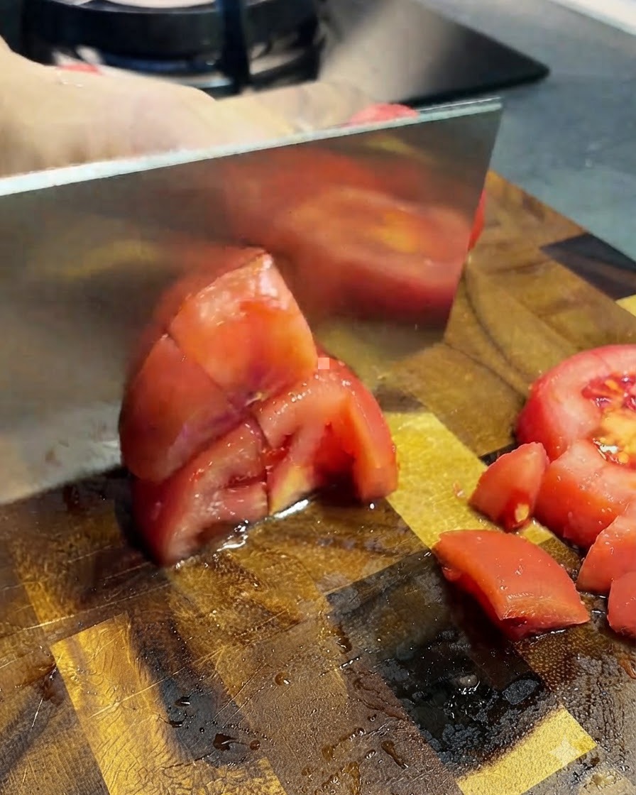 Tomates pelées coupées en petits morceaux avec un couperet sur une planche en bois.