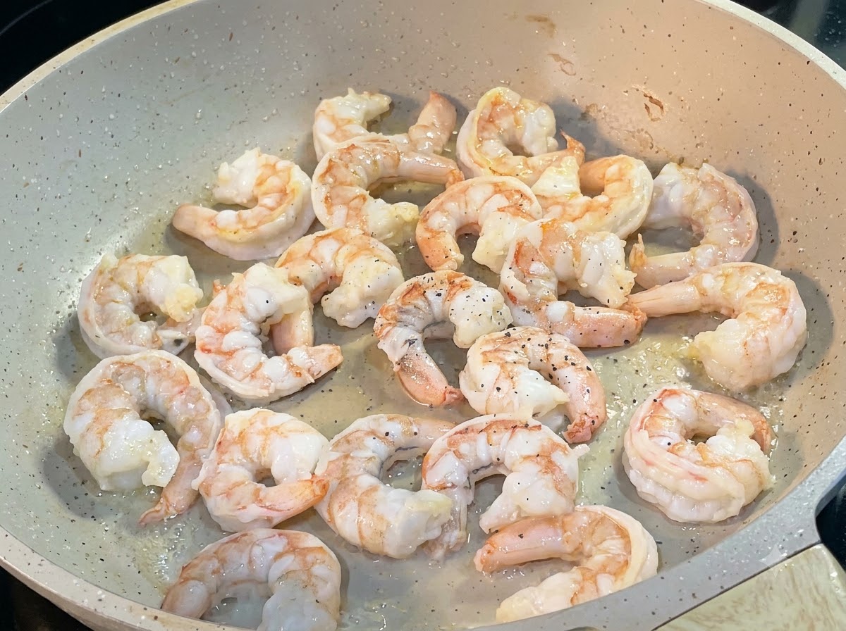 Crevettes sautant dans une poêle, saupoudrées de poivre noir.