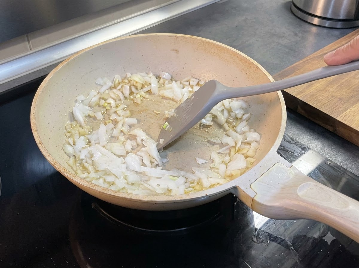 Oignons hachés mélangés dans du beurre fondu à lintérieur dune poêle à laide dune spatule.