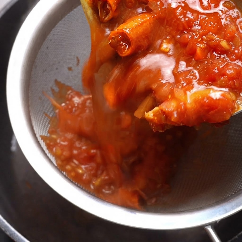 De la sauce tomate cuite versée à travers un tamis métallique avec une spatule pressant le contenu.