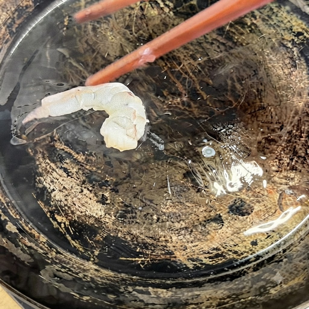 Des crevettes en papillon placées dans une poêle chaude huilée à laide de baguettes de cuisine.