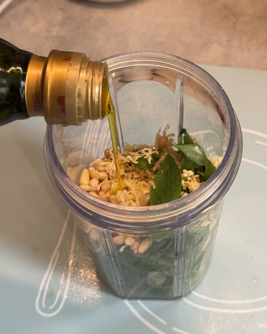 Huile dolive versée dune bouteille dans le bol du mixeur sur les ingrédients du pesto.