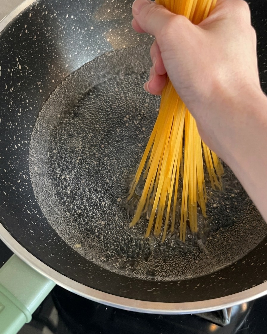 Nouilles de spaghetti sèches tenues par une main et plongées dans une casserole deau bouillante.