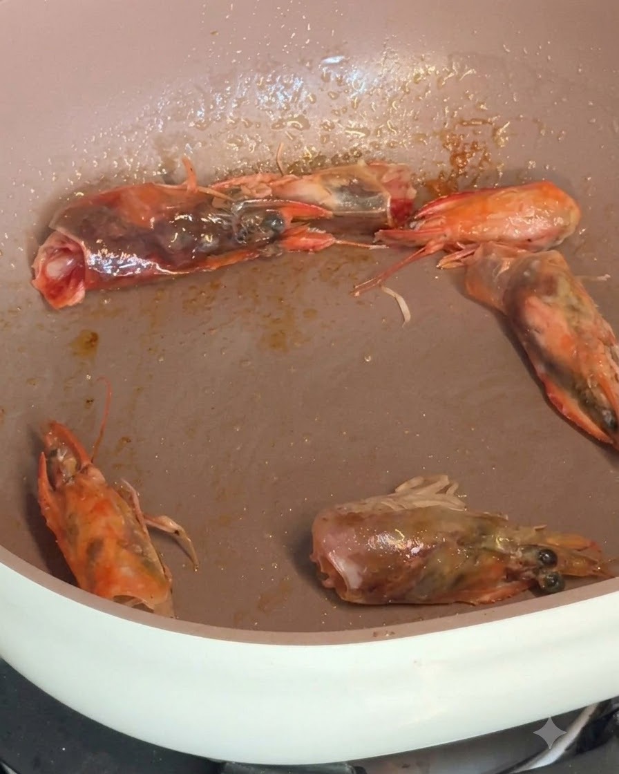 Crevettes décortiquées et têtes de crevettes qui grésillent dans une poêle tout en étant assaisonnées dépices.