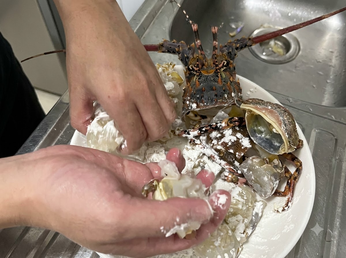 Mains remuant activement des morceaux de chair et de carapace de homard cru dans de la fécule de maïs blanche sur une assiette pour assurer un enrobage uniforme.