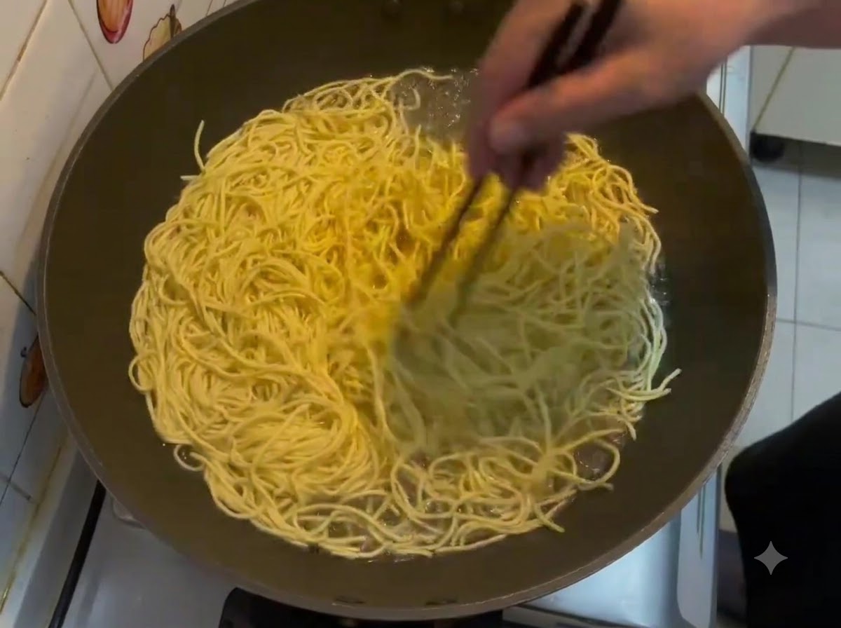 Baguettes remuant un grand lot de nouilles E-fu jaunes bouillant dans un wok.