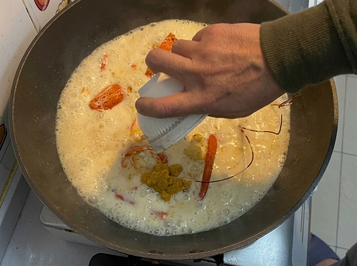 La pâte de homard jaune réservée versée dun petit bol blanc dans un wok avec des morceaux de homard frits et une sauce crémeuse.