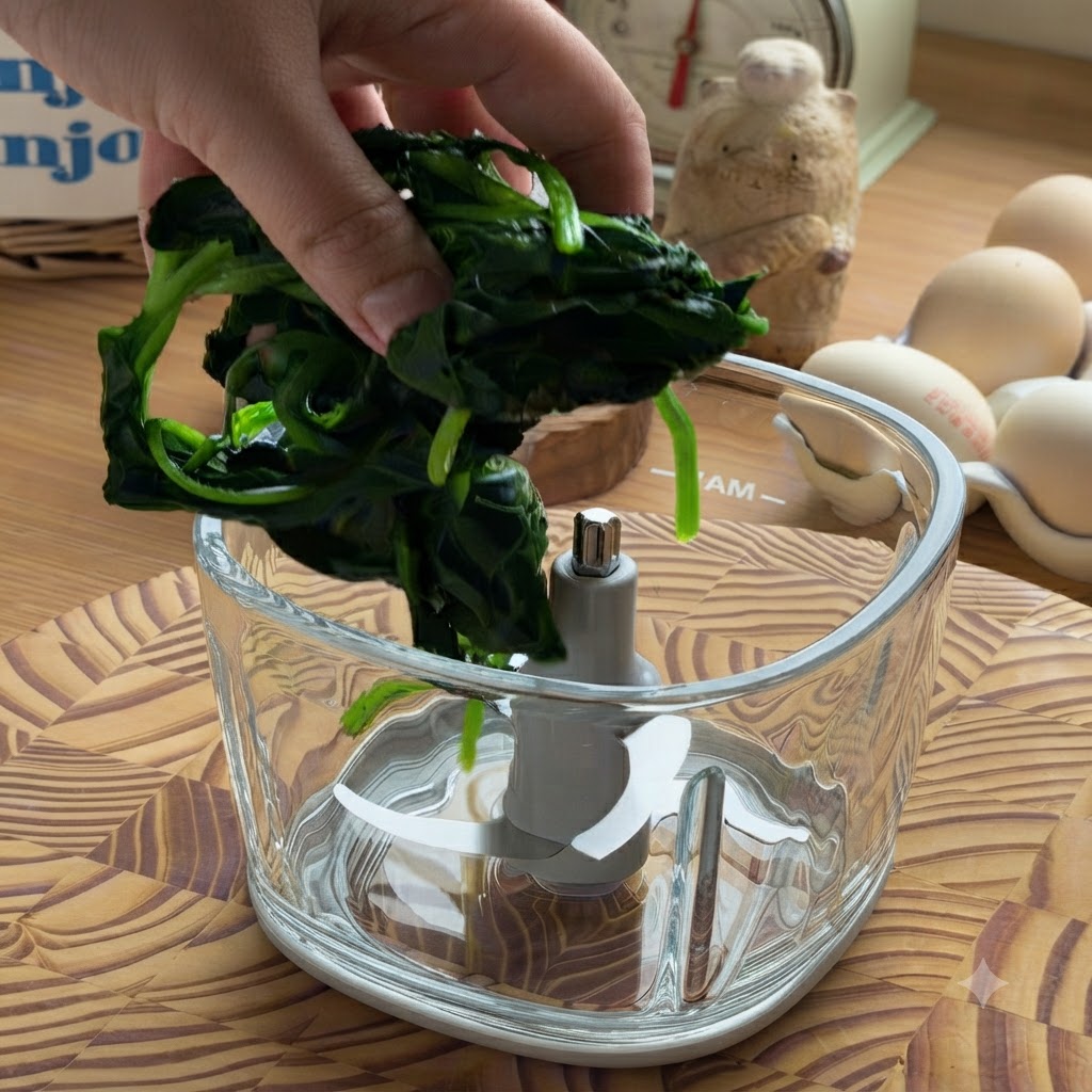 Une main plaçant une boule dépinards cuits et essorés dans le bol vide dun robot culinaire en verre.