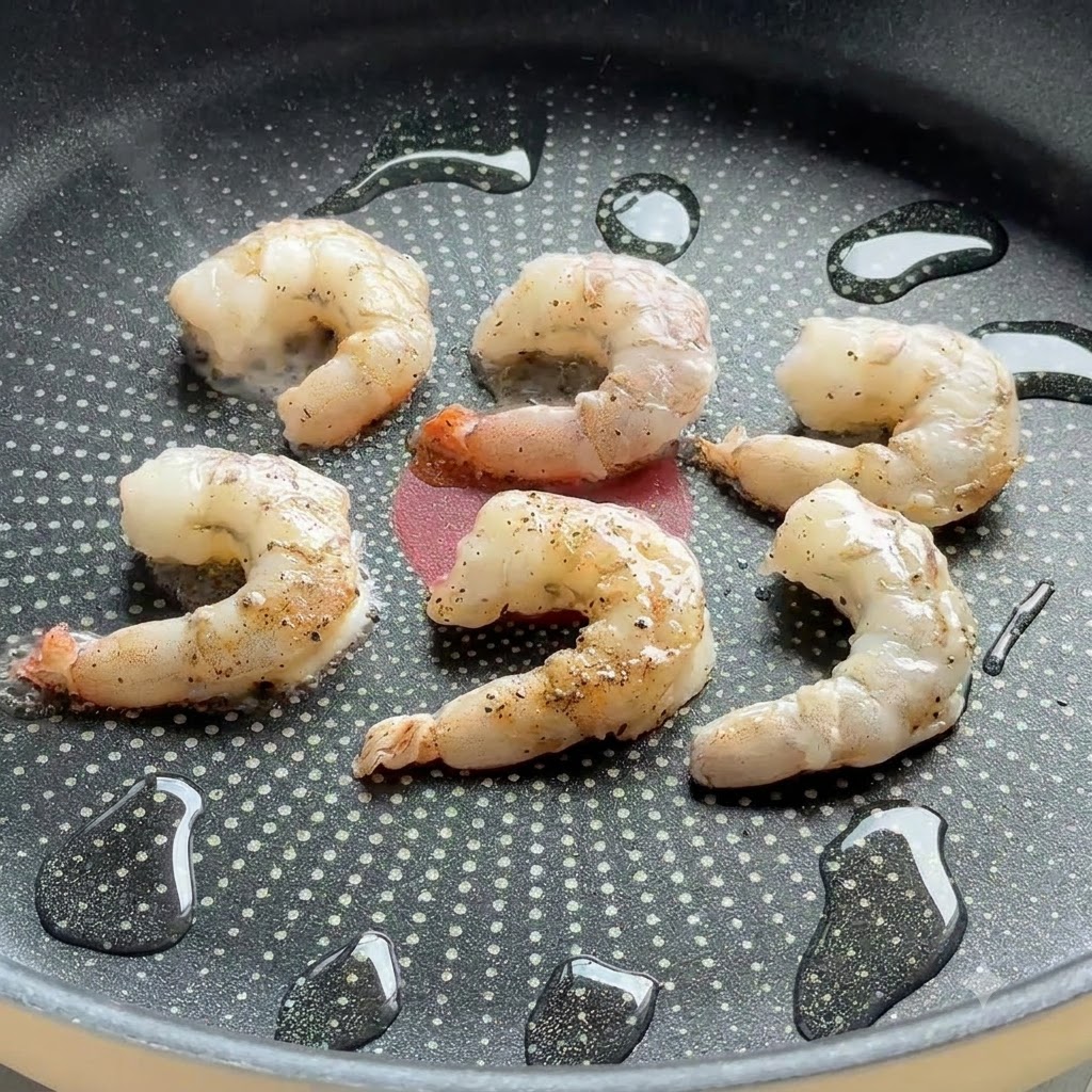 Des crevettes assaisonnées grésillant dans une poêle antiadhésive avec des gouttes dhuile.