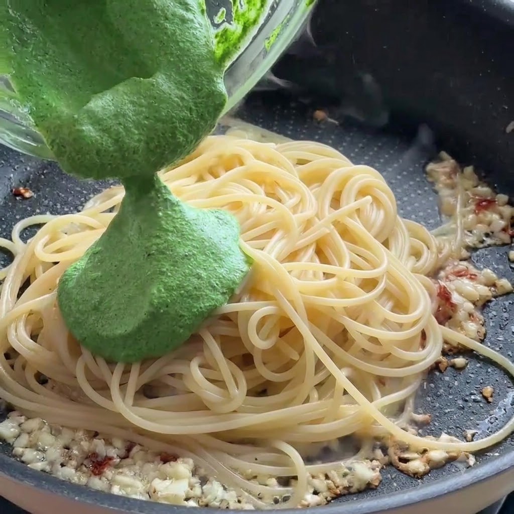 De la sauce pesto verte versée dun bol en verre sur des spaghettis dans une poêle.