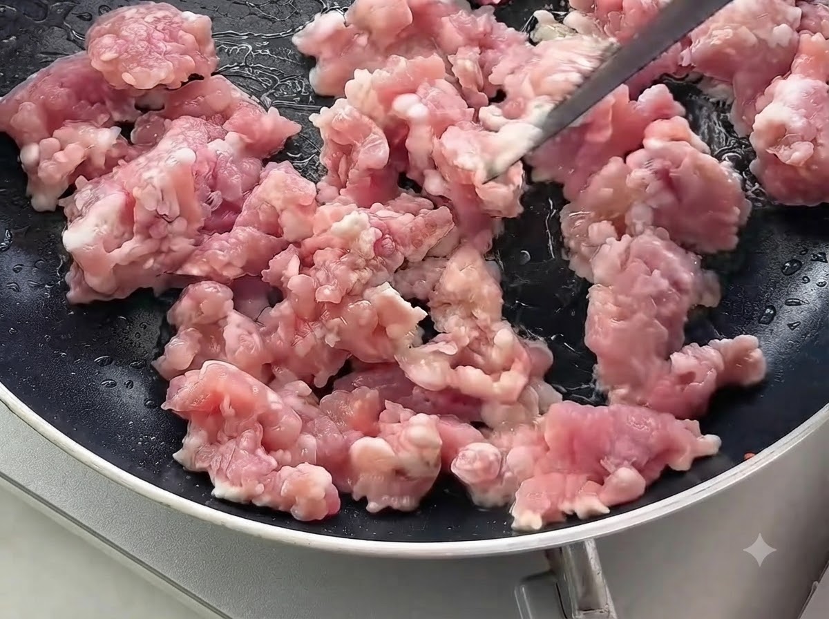 Du porc haché cru remué et cuit dans une poêle noire.