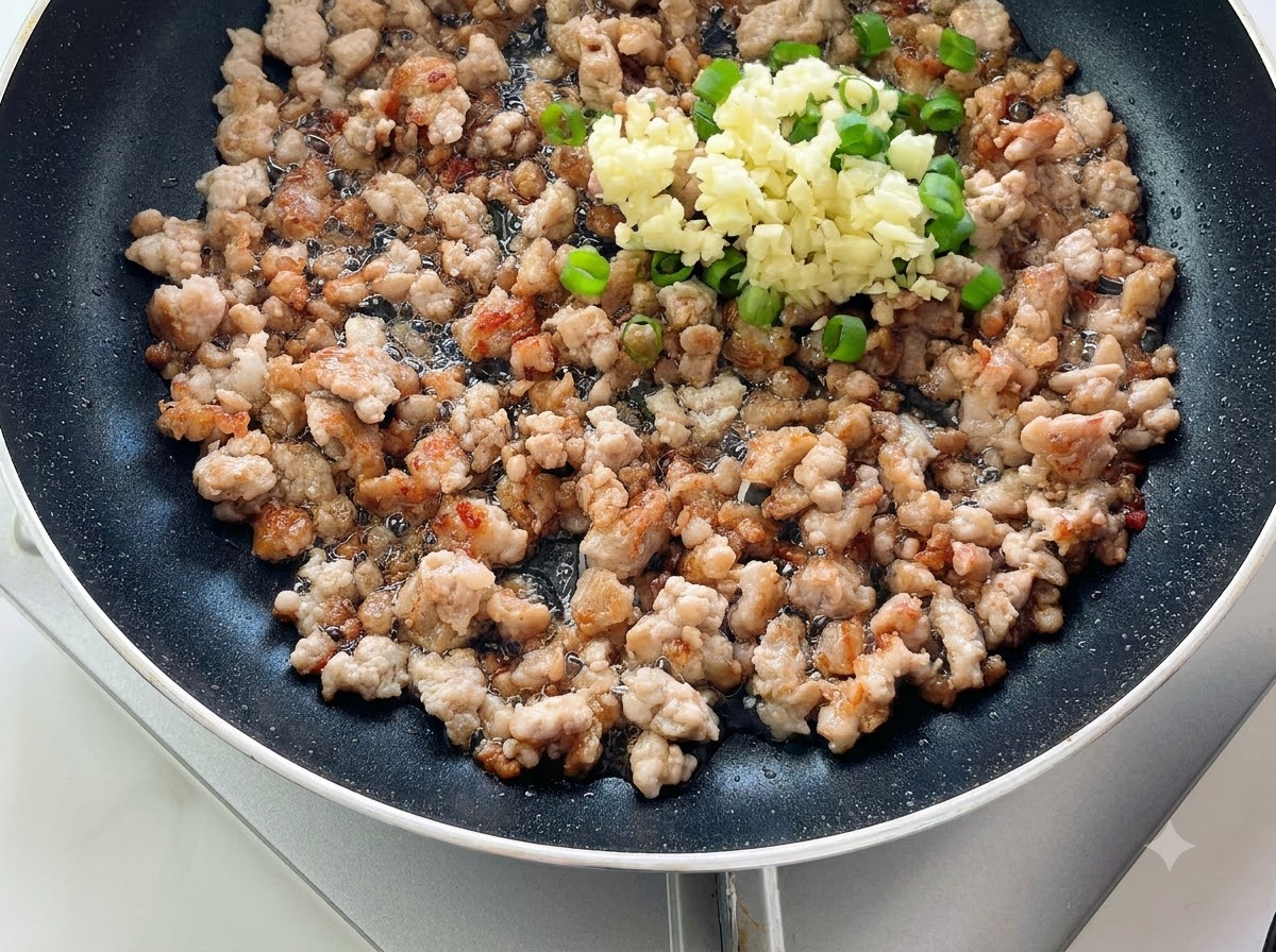 De lail haché et des oignons verts empilés sur la viande hachée cuite dans une poêle.