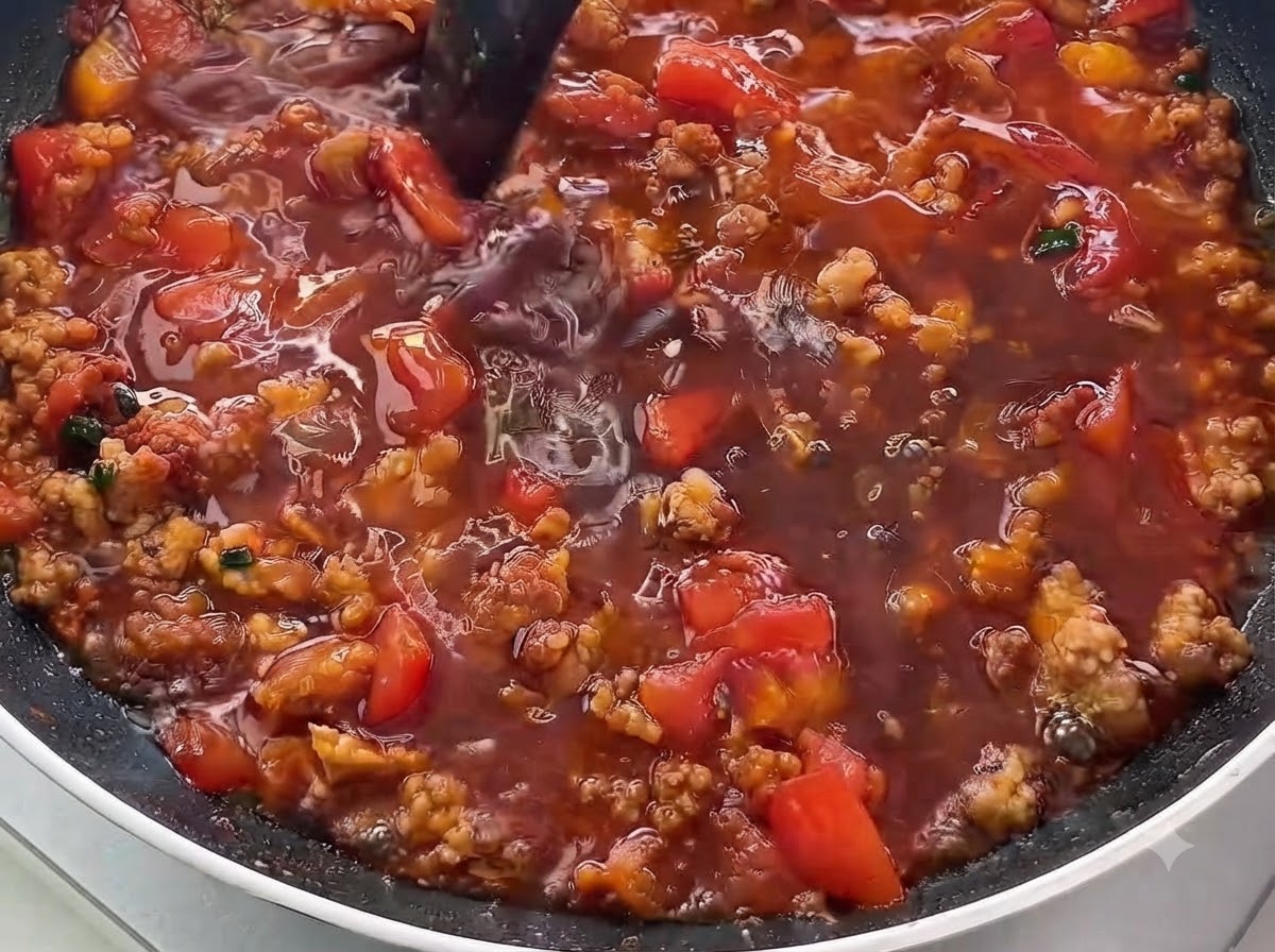 Gros plan dun liquide foncé versé dans une poêle remplie de viande hachée dorée et de dés de tomates.
