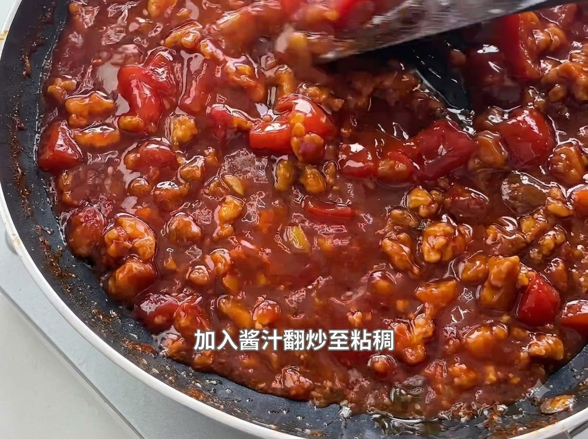 Une spatule remuant une sauce épaisse et bouillonnante à la tomate et à la viande hachée dans une poêle noire.