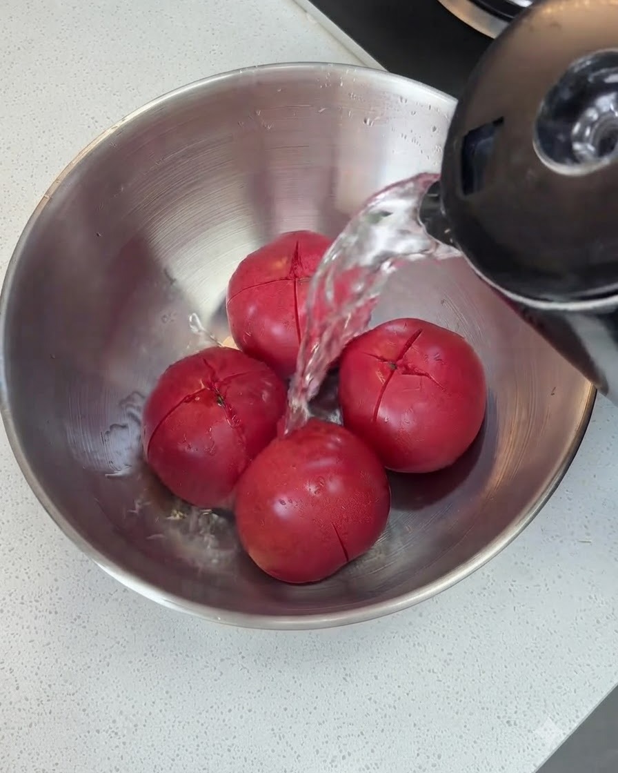 De leau chaude versée dune bouilloire sur des tomates incisées dans un bol en métal.
