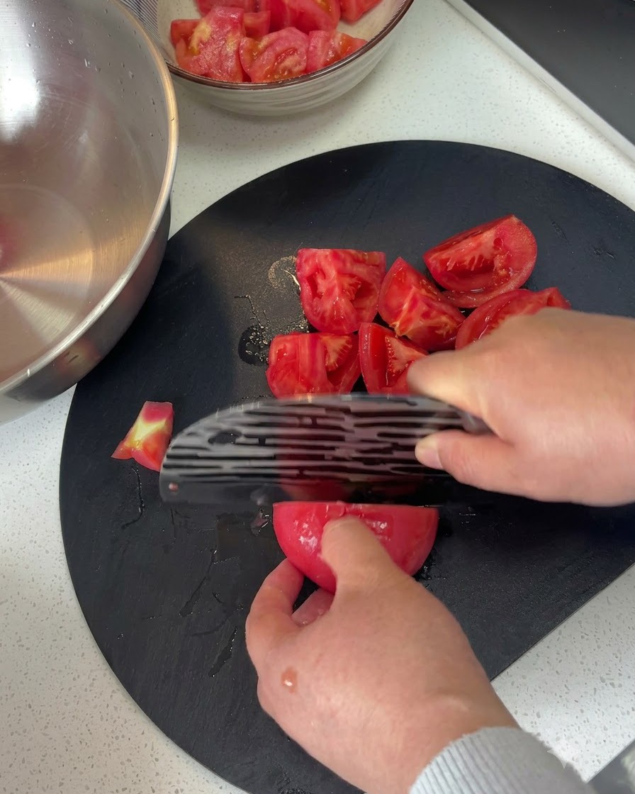Tomates pelées coupées en morceaux sur une planche à découper sombre avec un couteau.
