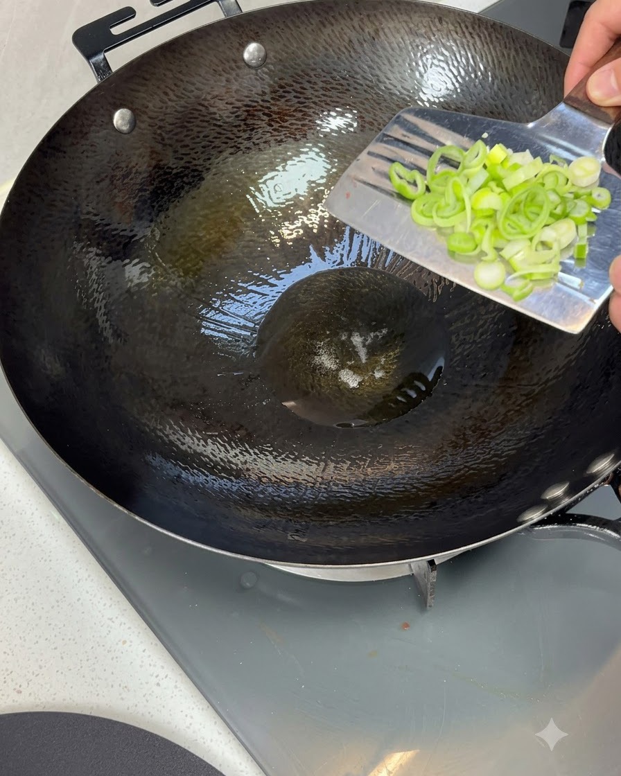 Oignons verts hachés déposés dans un wok chaud rempli dhuile de cuisson scintillante.