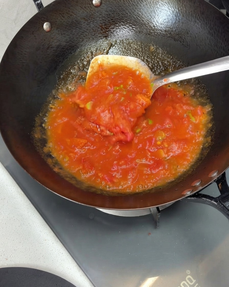Tomates écrasées et mélangées pour former une sauce riche dans un wok à laide dune spatule en métal.