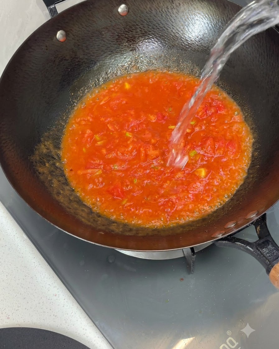 Eau versée den haut dans un wok rempli de sauce tomate cuite.