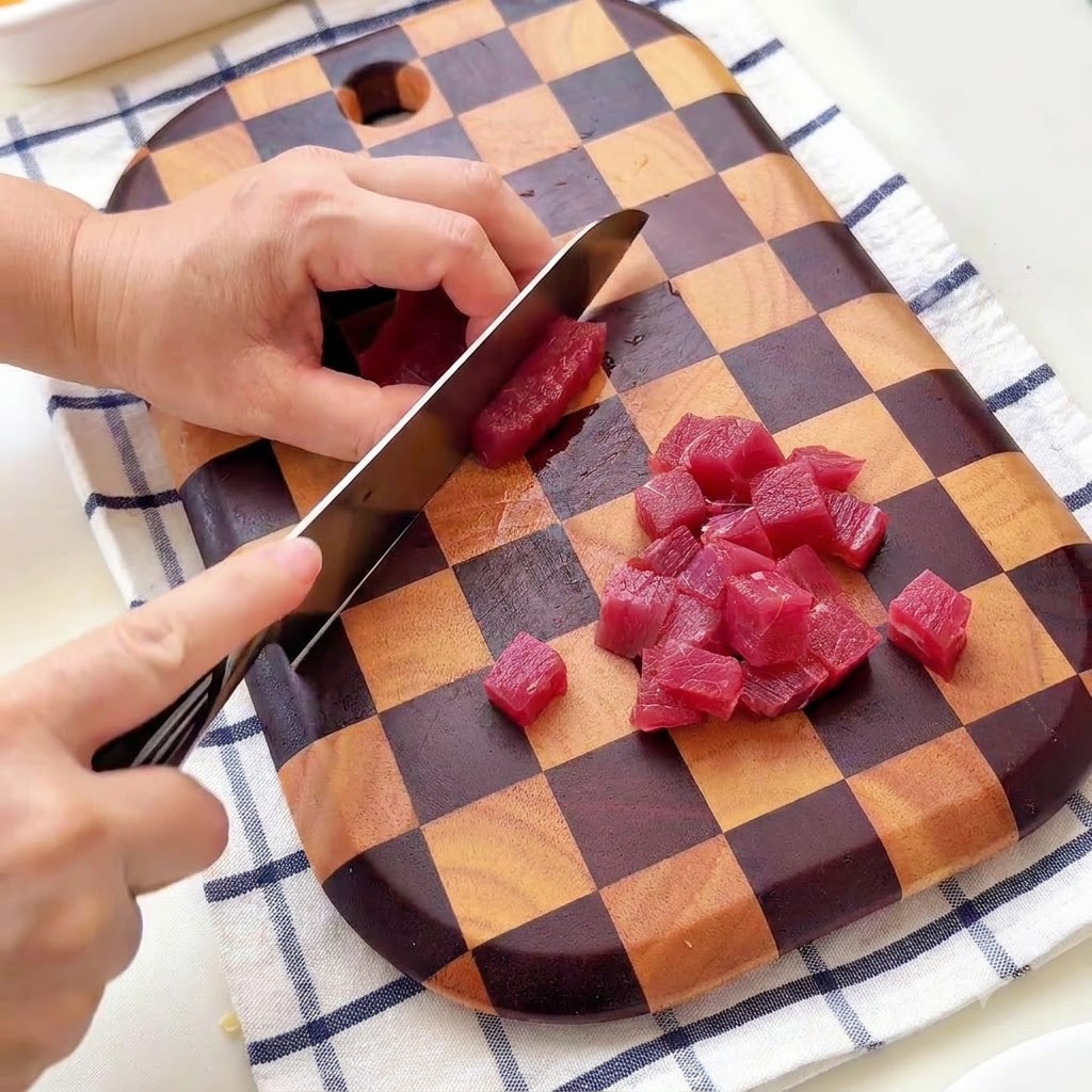 Une personne coupant du bœuf en petits cubes sur une planche a decouper en bois a damier.