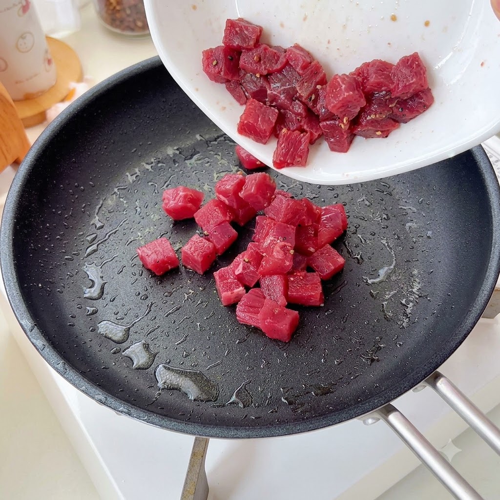 Des cubes de bœuf assaisonnes verses et sautes dans une poele.
