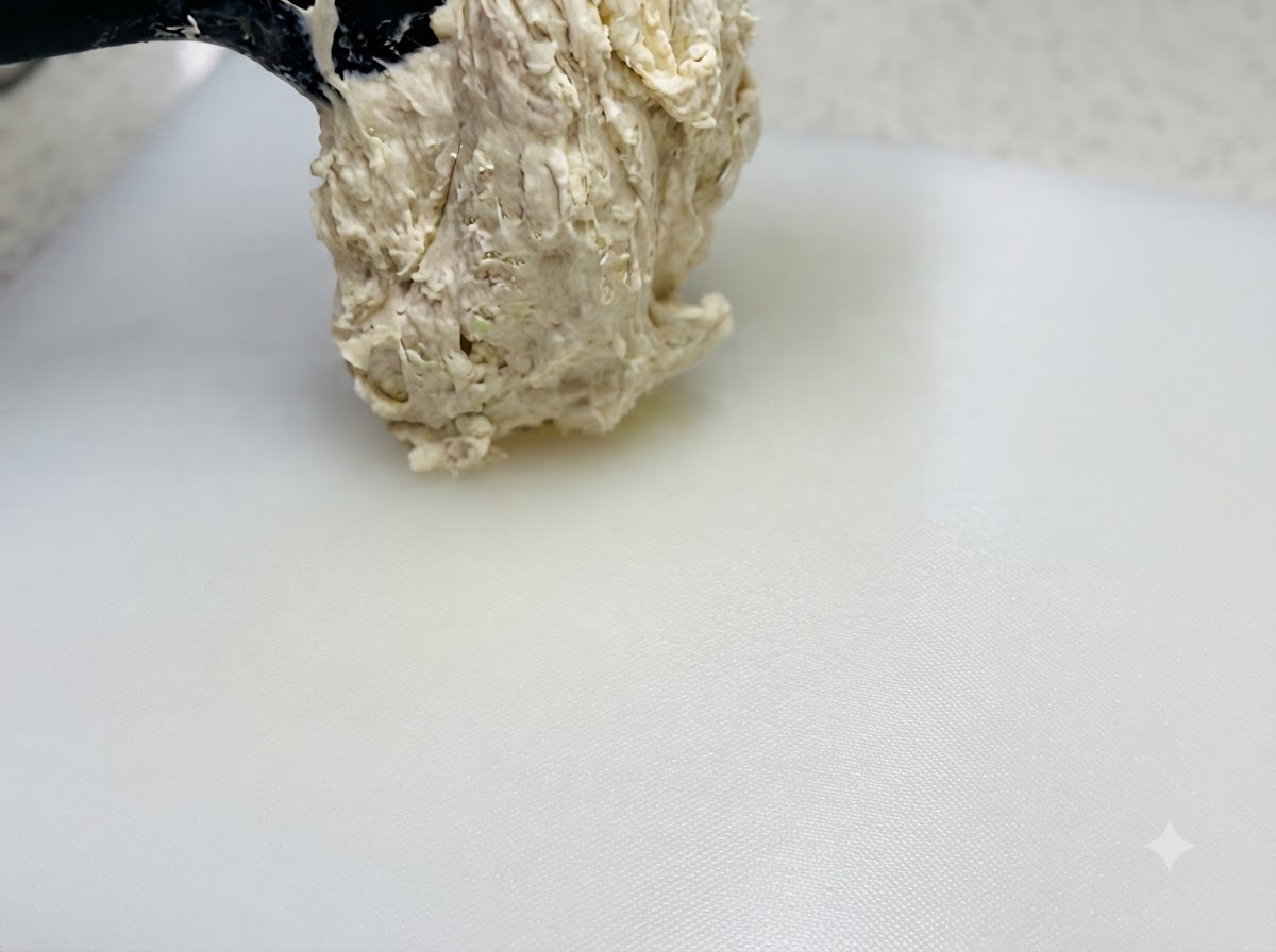 Pâte très hydratée et collante soulevée avec une spatule et déposée sur une planche à découper blanche huilée.