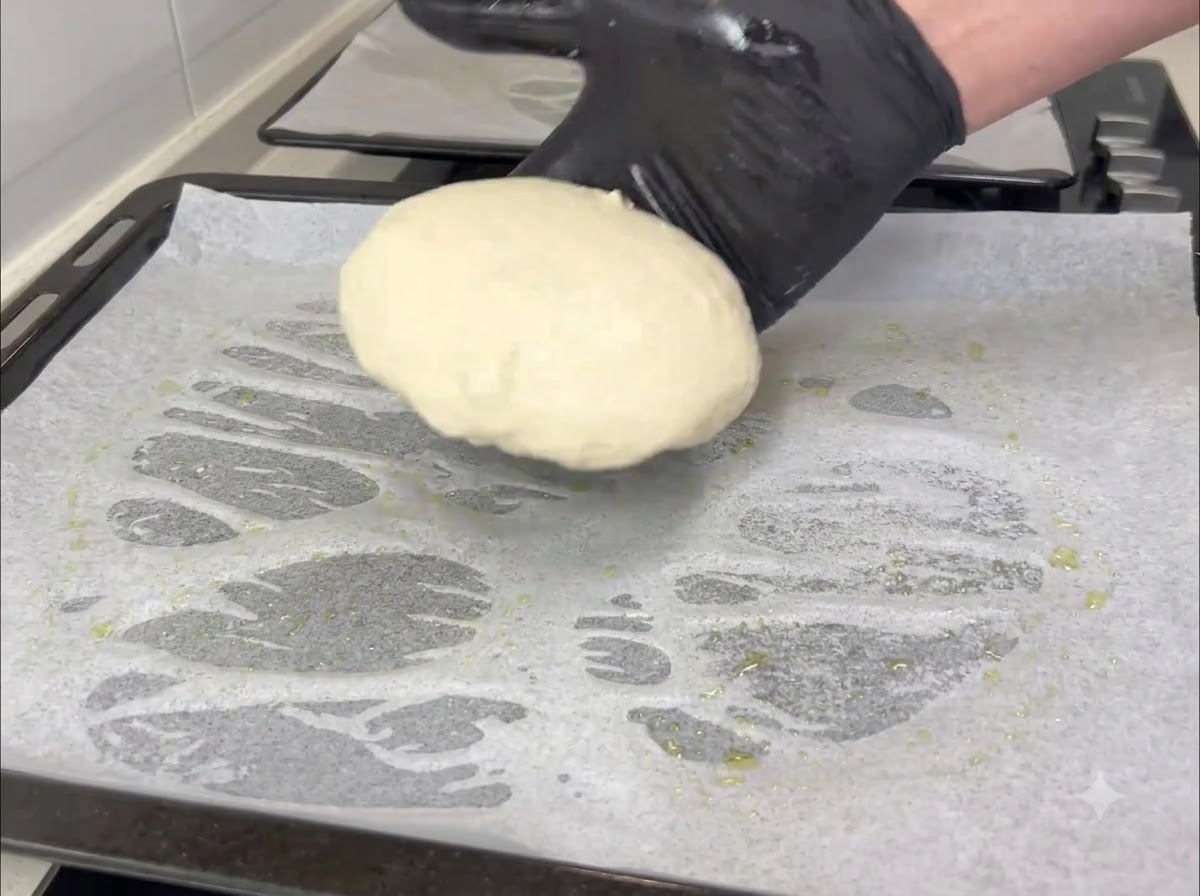 Main gantée transférant un pâton rond sur une plaque de cuisson recouverte de papier sulfurisé.