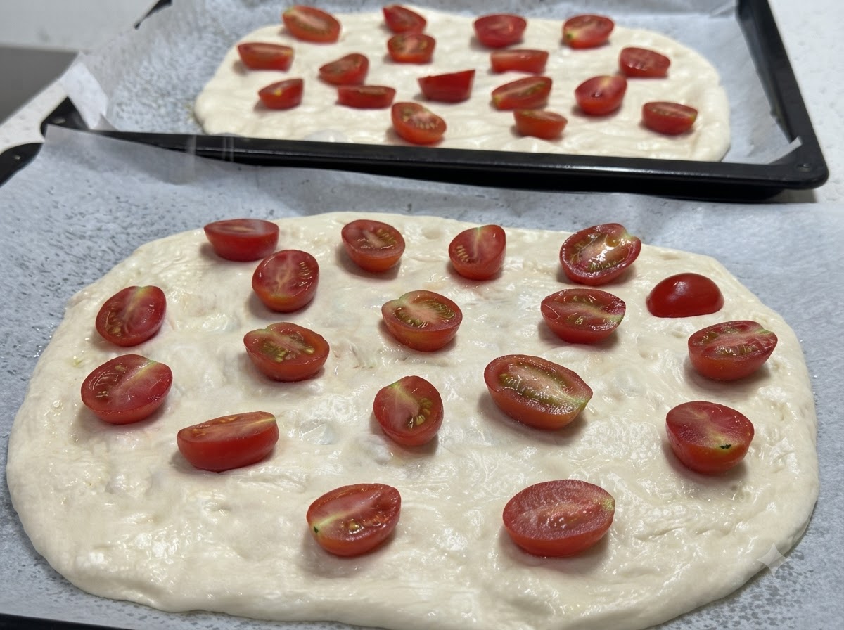 Gros plan sur deux fonds de pâte à pizza étirés, garnis de tomates cerises coupées en deux, prêts à être assaisonnés.