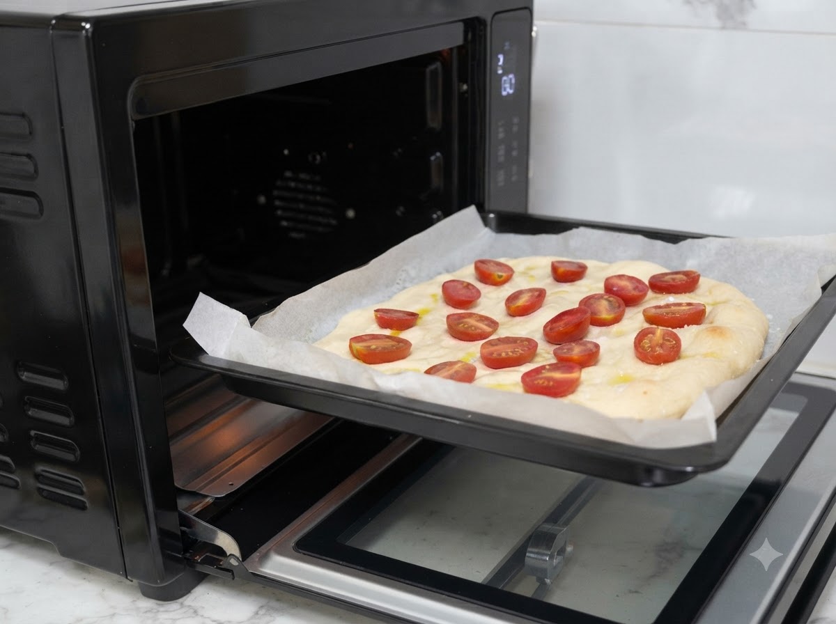 Une plaque de cuisson avec la pâte à pizza garnie glissée dans un four noir.