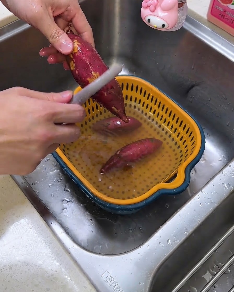Une personne épluchant des patates douces crues au-dessus dun évier de cuisine à laide dun économe.
