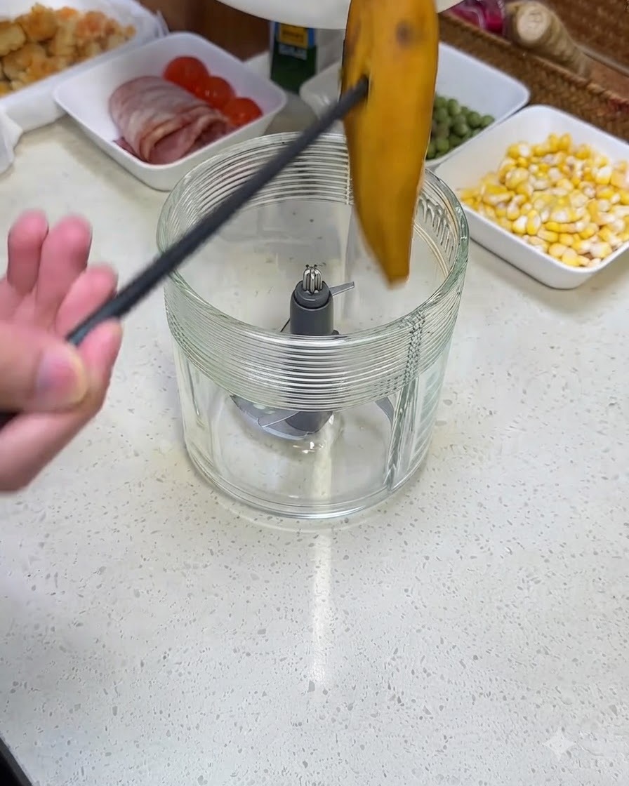 Une personne utilisant des pinces noires pour déposer une patate douce cuite dans le bocal en verre dun blender.