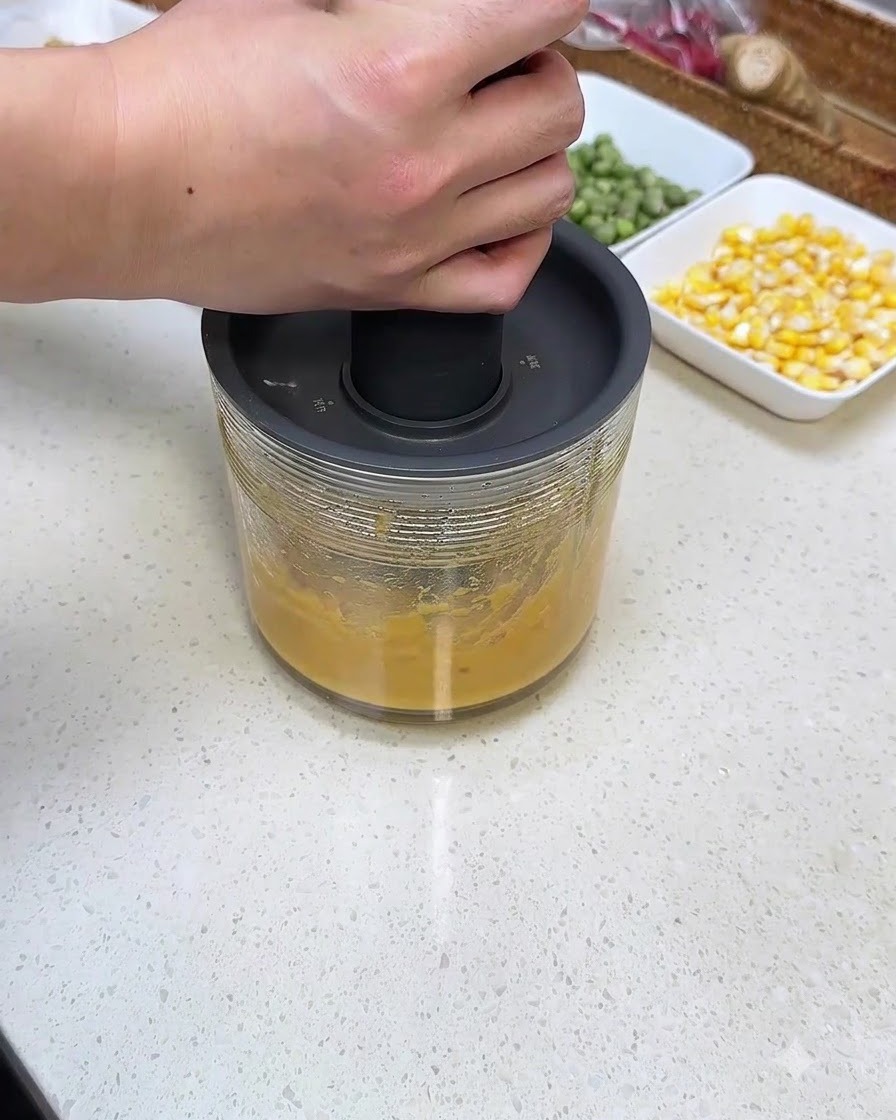 Une personne appuyant sur un mixeur plongeant manuel au-dessus dun récipient en verre rempli de purée de patate douce.