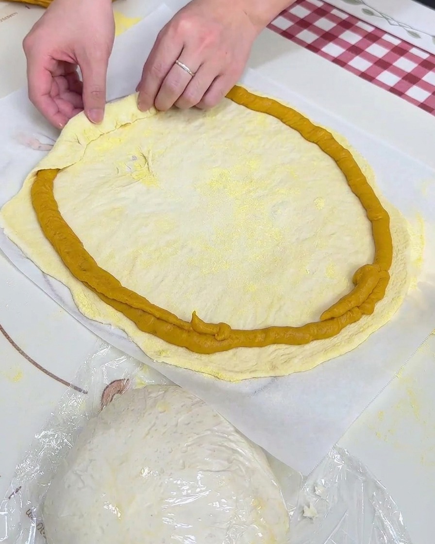 Des mains repliant le bord de la pâte sur lanneau de purée de patate douce pochée sur du papier sulfurisé.