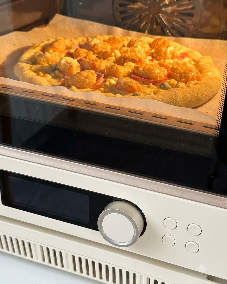 Une pizza assemblée sur du papier sulfurisé en train dêtre enfournée, lintérieur du four brillant dun orange chaleureux.
