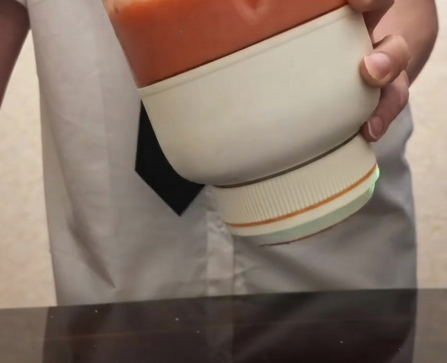 Une personne tenant un blender electrique portable rempli dune puree de tomate rouge et lisse.