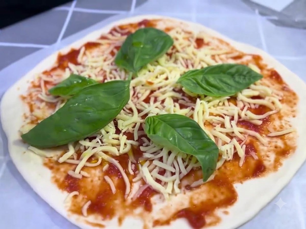Une pizza assemblée garnie de fromage et de feuilles de basilic recevant un léger filet dhuile dolive.