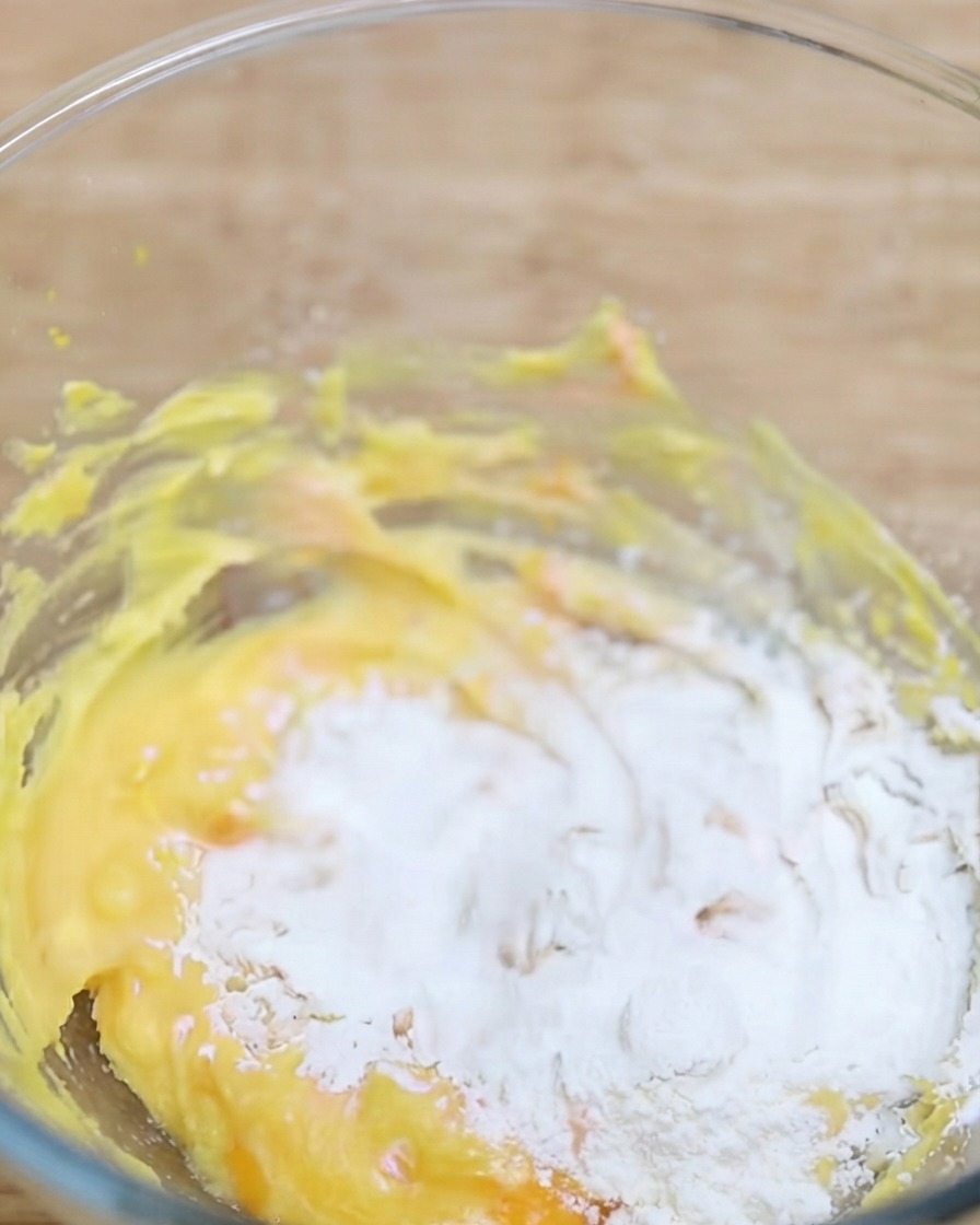 De la poudre de matcha tamisée dans un bol contenant la base de pâte jaune.