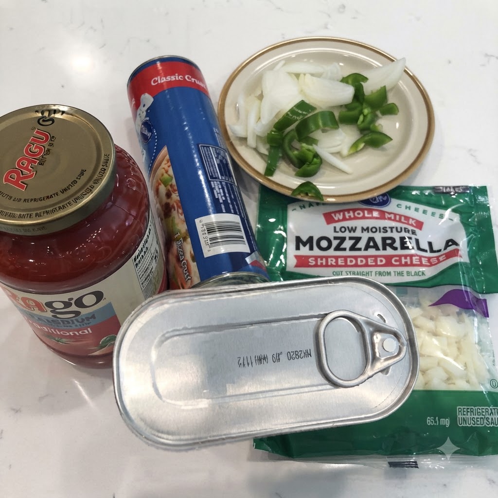 Une boîte danchois, un pot de sauce marinara, de la pâte à pizza en conserve, de la mozzarella râpée et des oignons et poivrons tranchés sur un comptoir blanc.