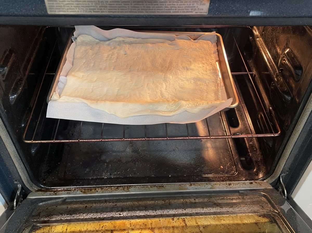Une plaque de cuisson avec de la pâte à pizza crue sur du papier sulfurisé placée sur la grille du four à lintérieur dun four préchauffé.