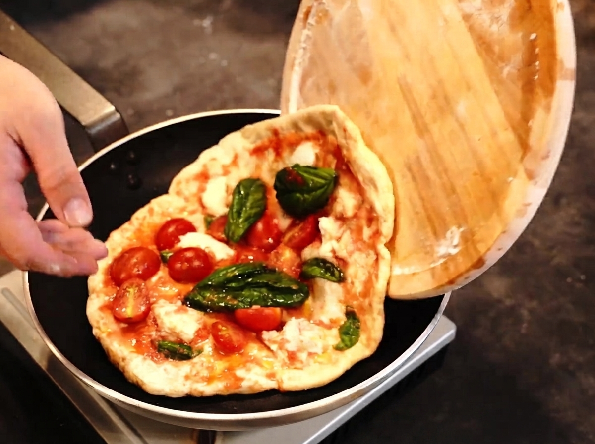Une pizza transférée dune pelle en bois à une poêle avec un chalumeau à proximité.
