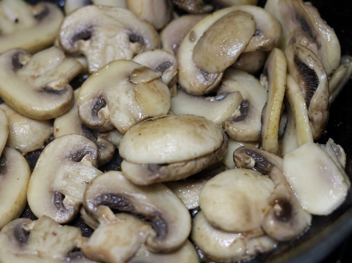 Des tranches de champignons de Paris blancs qui grésillent et cuisent dans une poêle avec de la crème légère.