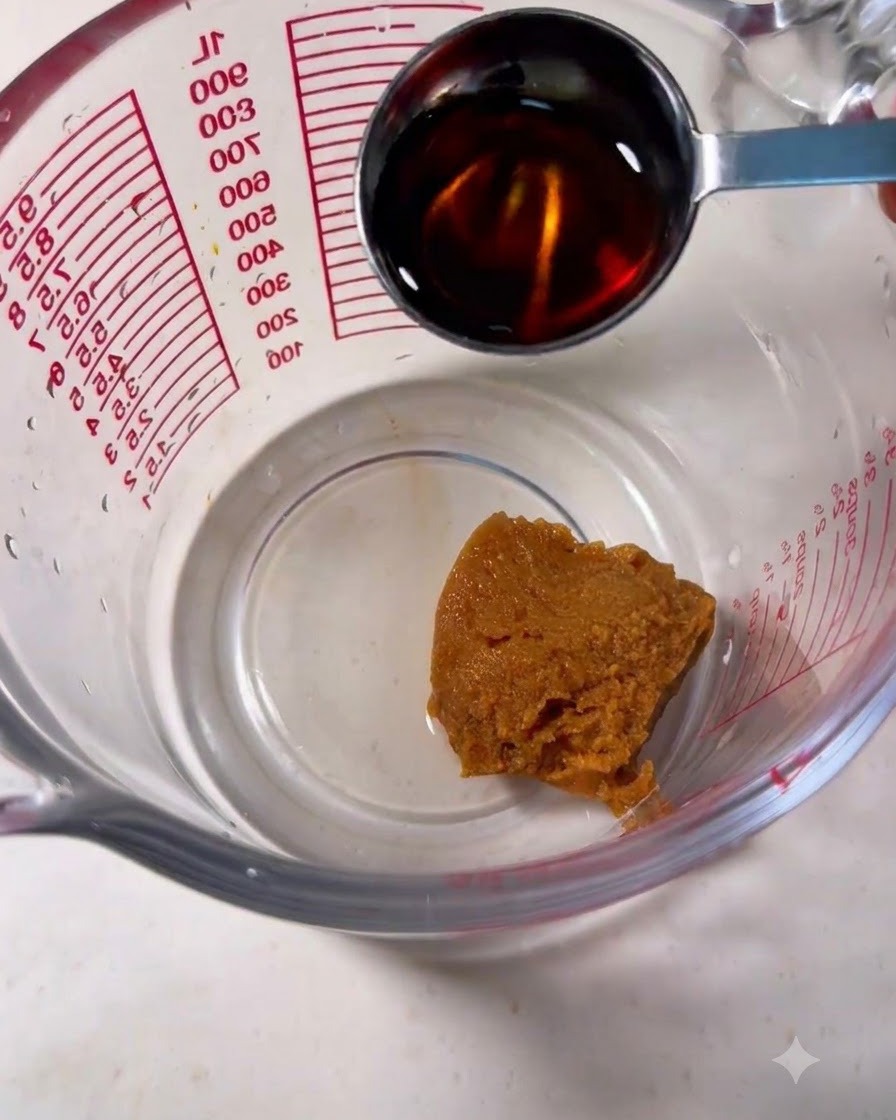 Un verre doseur contenant de la pâte miso brune et une cuillère y versant du mirin.