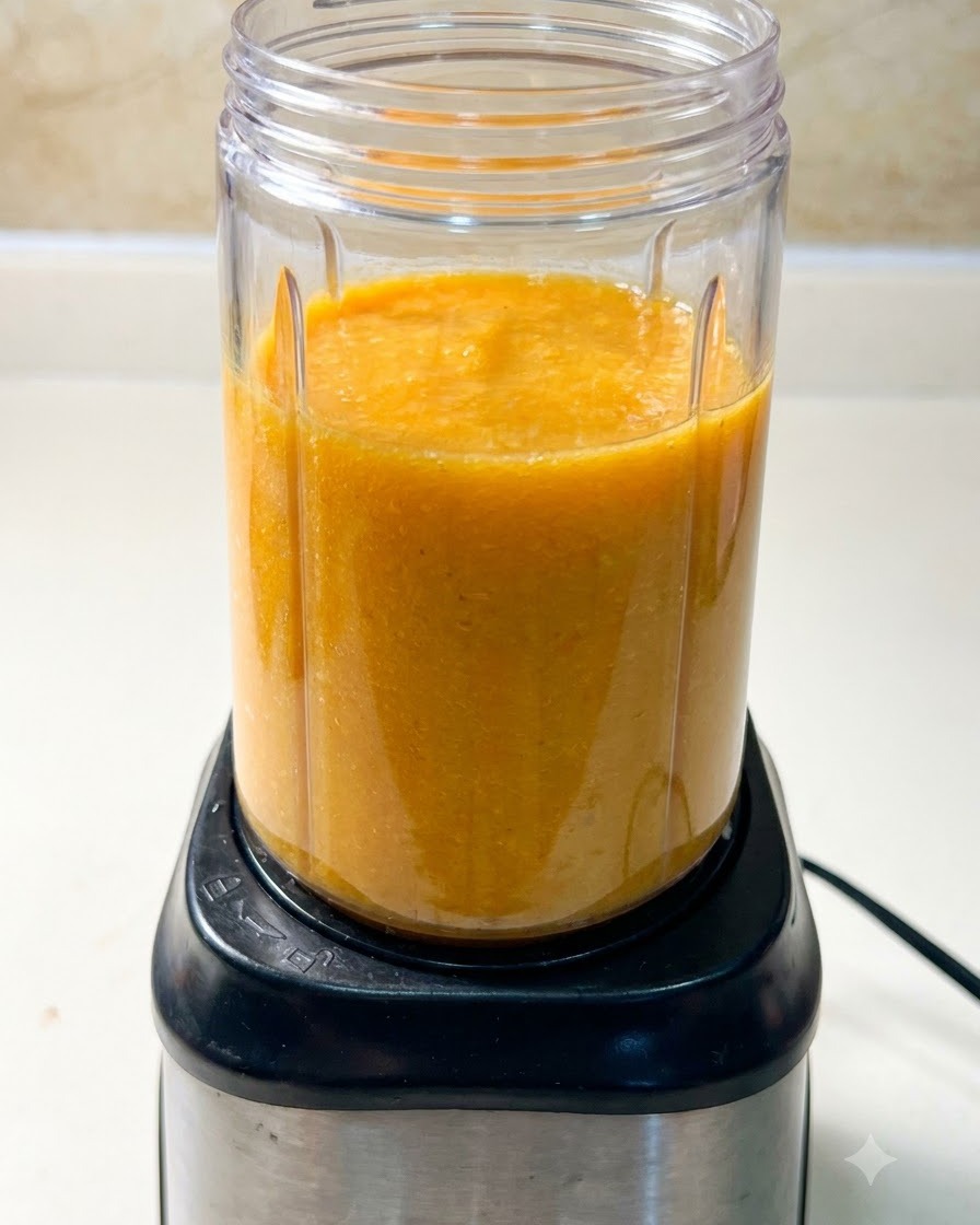 Un bol mixeur rempli dun mélange de soupe orangé posé sur le socle noir du blender.