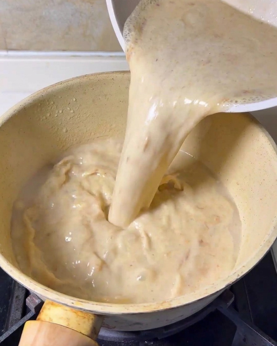 Une base de soupe crémeuse et mixée est versée dun récipient dans une casserole jaune sur une cuisinière.