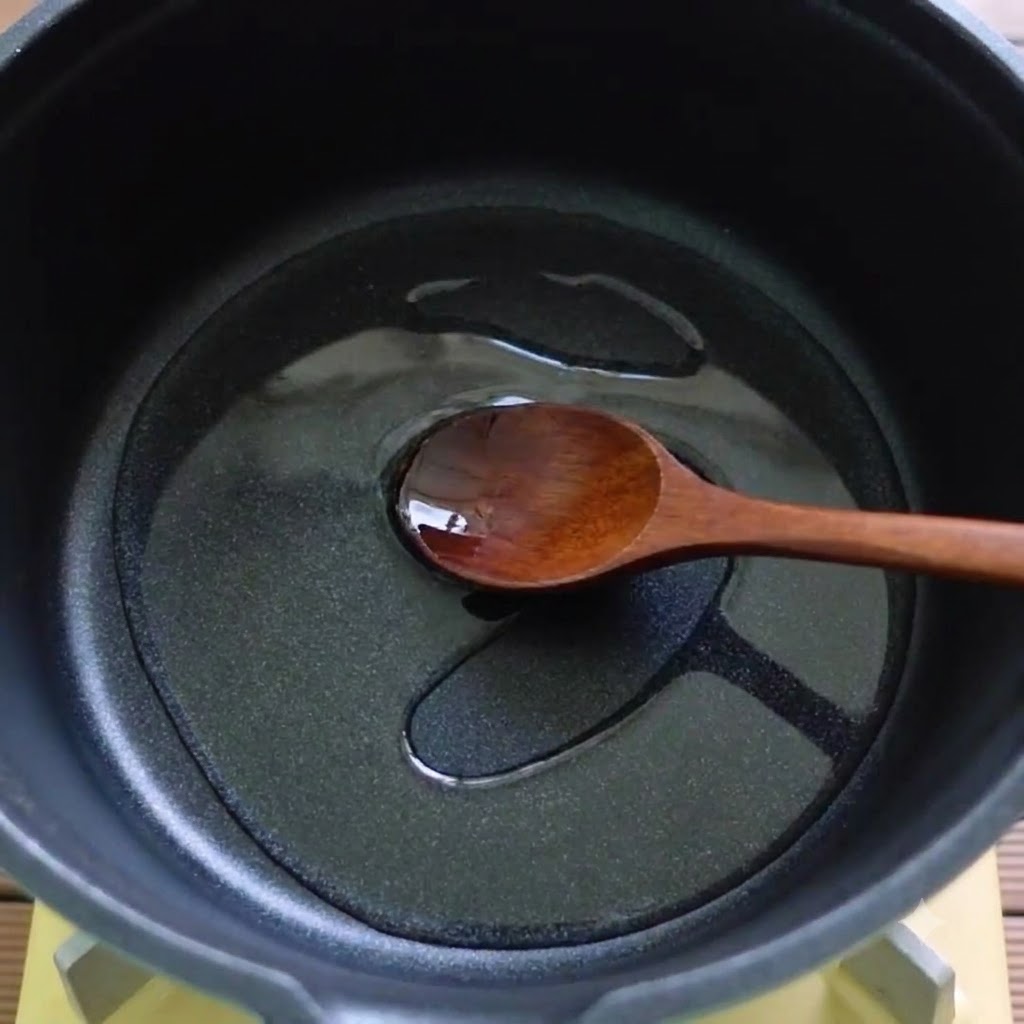 Une cuillère en bois remuant de lhuile et des ingrédients fondus dans une casserole noire.