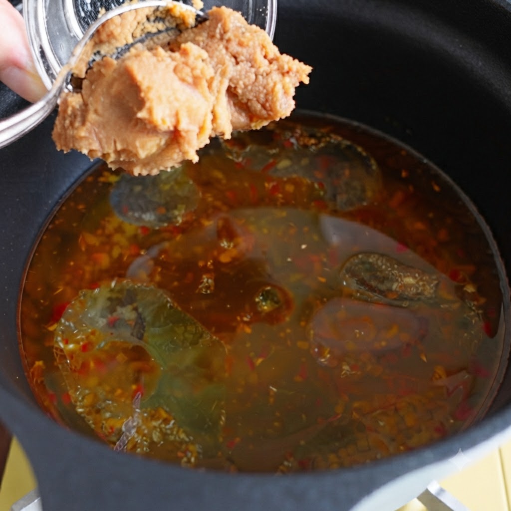 De la pâte de miso ajoutée dans une casserole de bouillon assaisonné.