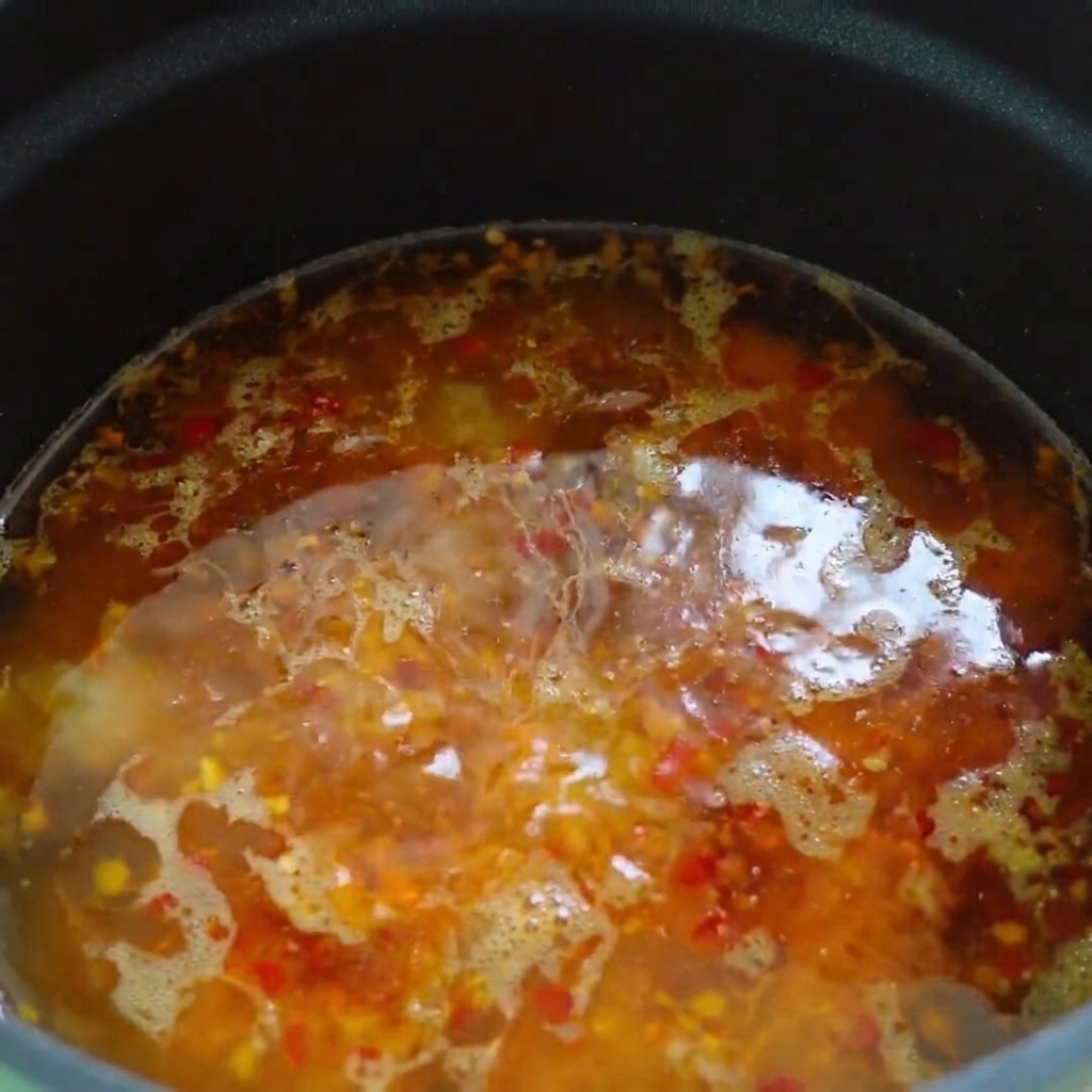 De lhuile pimentée et de lhuile de sésame versées en filet à la surface de la base de soupe chaude.